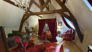 A cozy, well-lit attic bedroom with a sloped ceiling, a red carpet, and a canopy bed.