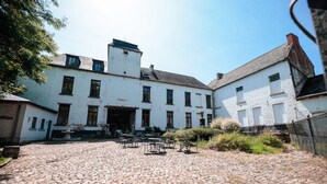 A courtyard with cobblestone paving, a white building with multiple windows, and outdoor seating.