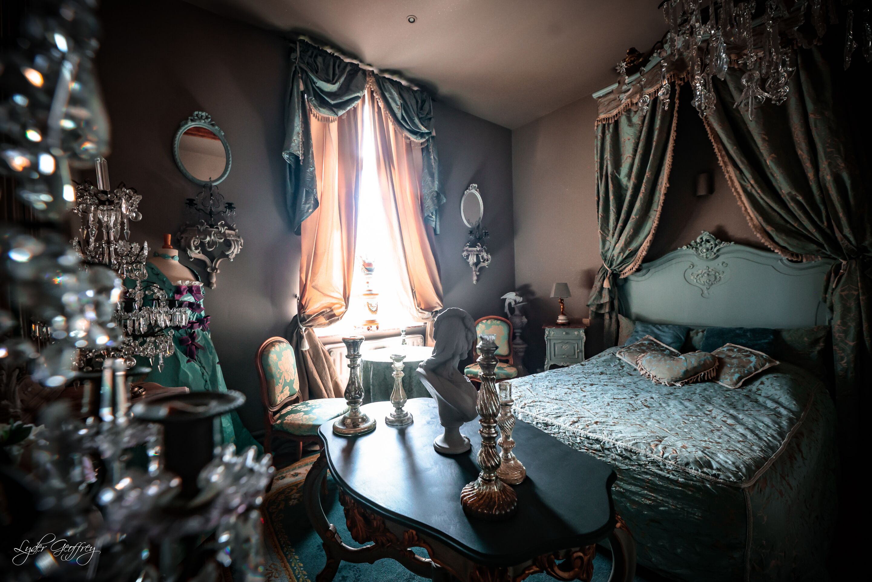 Une chambre à coucher de style vintage, avec des meubles richement décorés, un lustre et un grand miroir.