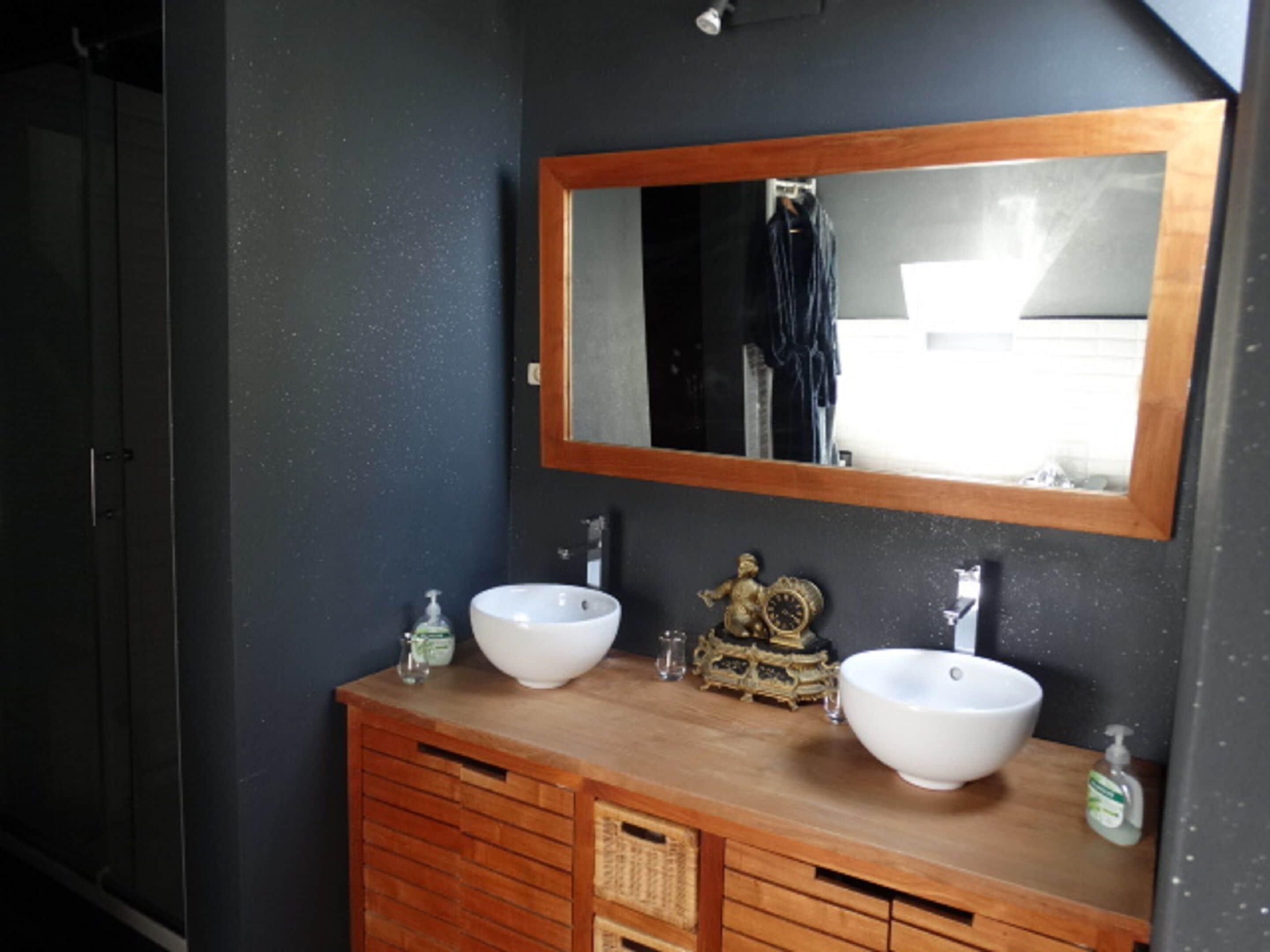 A bathroom with two sinks, a wooden vanity, a mirror, and a small decorative item.