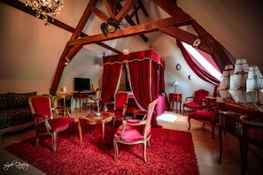 A room with a high ceiling, wooden beams, a red carpet, and a canopy bed. There are several chairs and a table with a lamp. - Le Domaine Du Château Blanc à 10 minutes de Pairi Daiza (Jurbise)