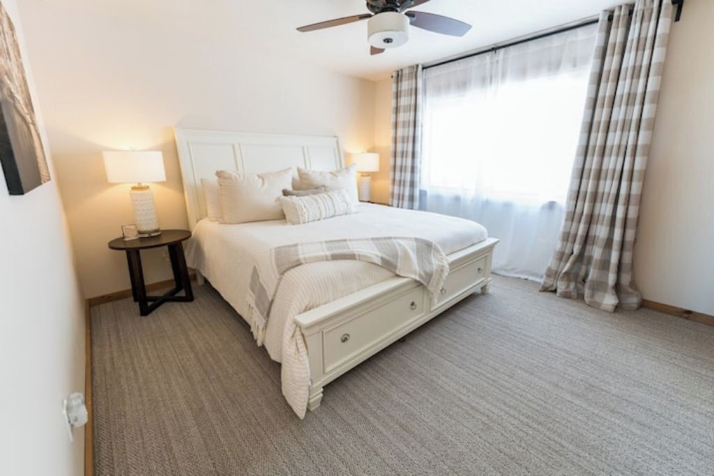 A neatly arranged bedroom with a bed, bedside tables, a ceiling fan, and a window with curtains.