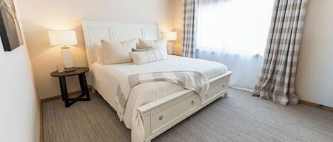 A neatly arranged bedroom with a bed, bedside tables, a ceiling fan, and a window with curtains.