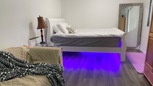 Quarto com uma cama, mesa de cabeceira com abajur, espelho e um sofá.