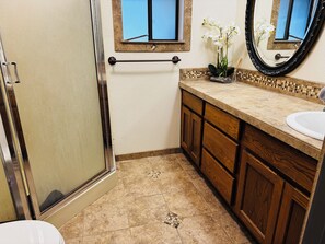 A bathroom with a shower, a sink, wooden cabinets, a mirror, and a window.
