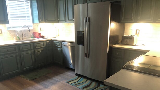 Una cocina con suelo de madera, un refrigerador de acero inoxidable, un lavavajillas y un tostador.