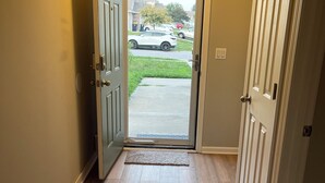 Un pasillo con suelo de madera, un felpudo en la entrada y una puerta que da al exterior.