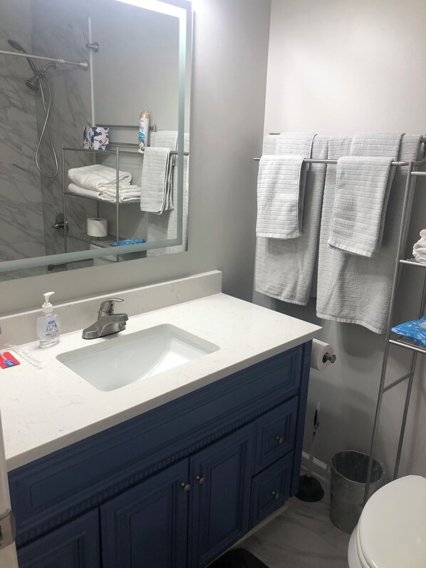 Une salle de bain avec un lavabo blanc, des meubles bleus, un miroir et un porte-serviettes avec plusieurs serviettes.