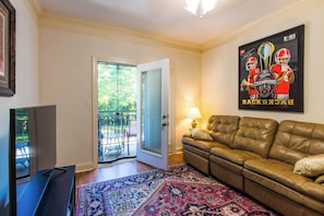 A living room with a leather sofa, a television, a patterned rug, a door leading to a balcony, and a poster on the wall. - Low Country Dawg House Stunning Walking Trails! (Athens)
