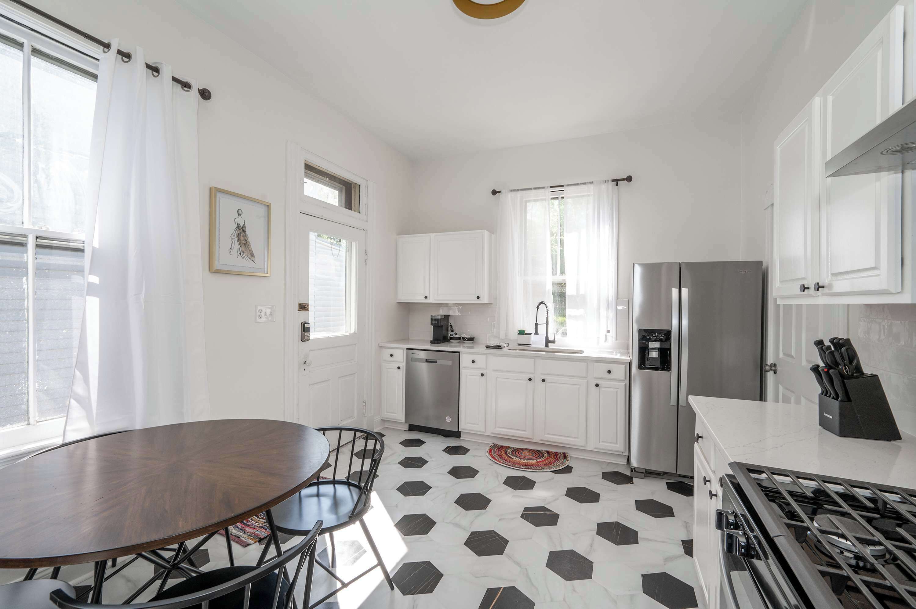 A modern kitchen with white cabinets, a stainless steel refrigerator, a gas stove, and a dining area with a round table and chairs.
