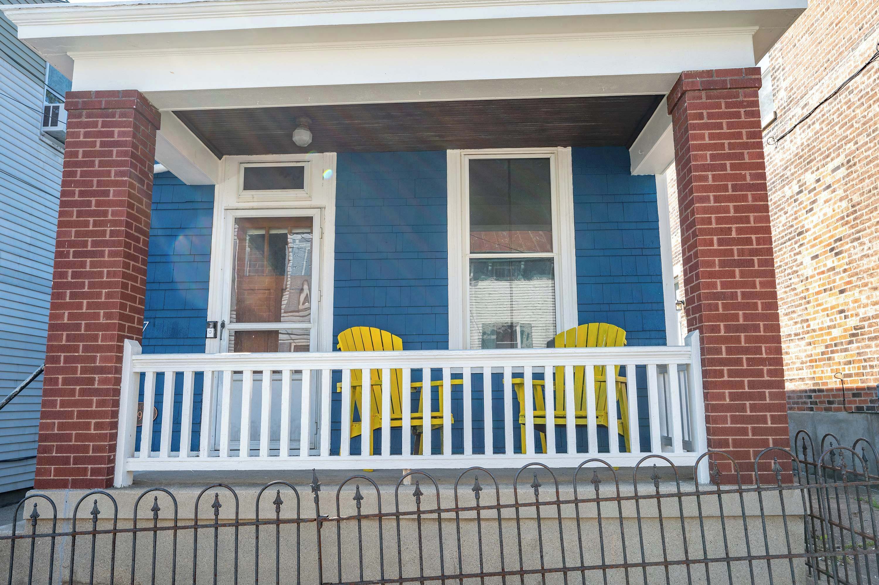 A blue house with a white porch and yellow chairs.