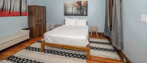 A bedroom with a wooden bed, a sofa, a wardrobe, and a painting on the wall.