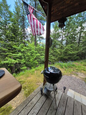 A wooden deck with a barbecue grill, an American flag, and a forested backdrop.