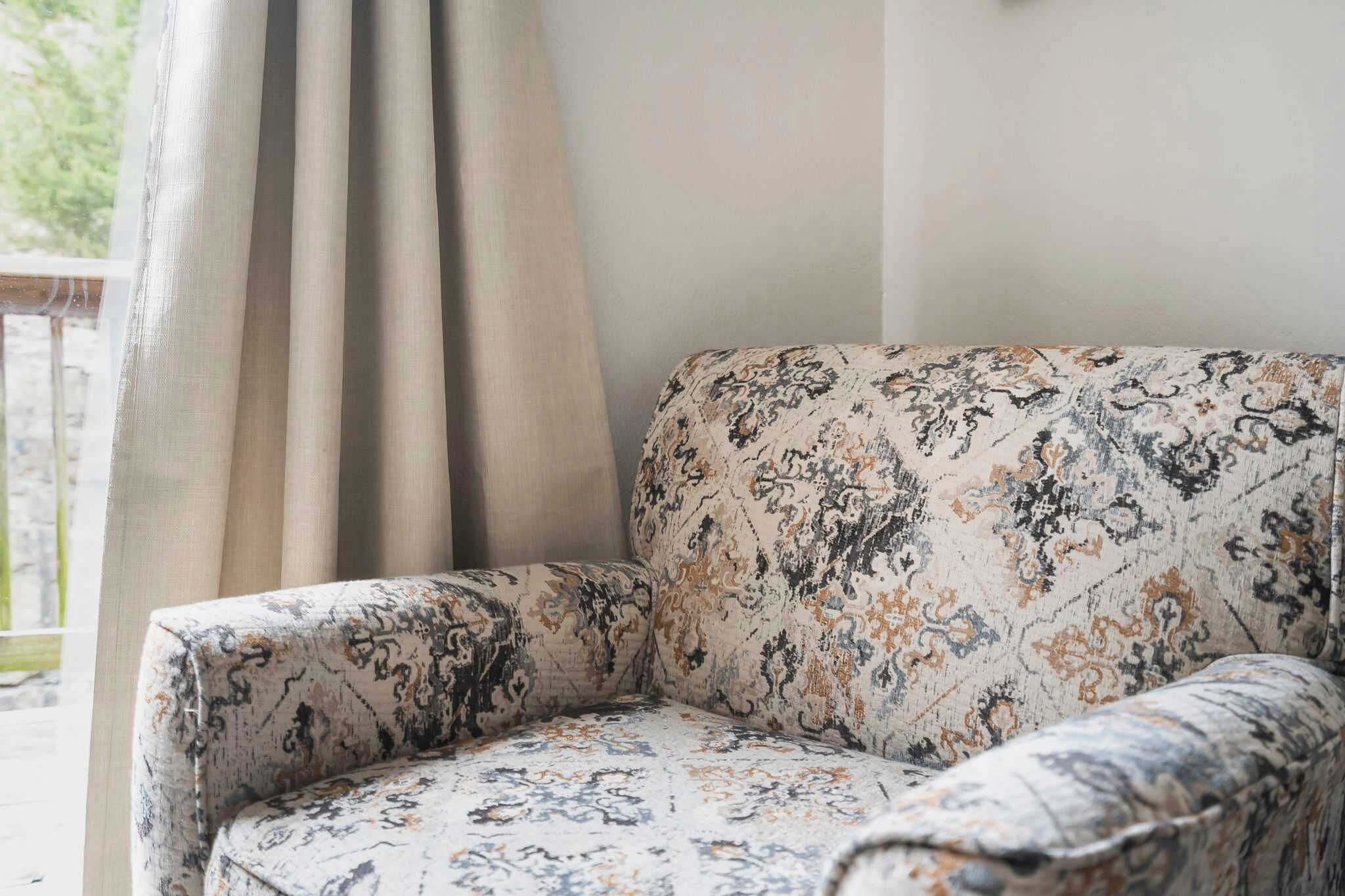 A corner of a room with a patterned sofa and a curtain.