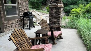 Two Adirondack chairs with pink cushions on a concrete patio, a stone pillar, and a grill in the background. - Mountain Apartment, Minutes to Resorts & Services (Ogden)