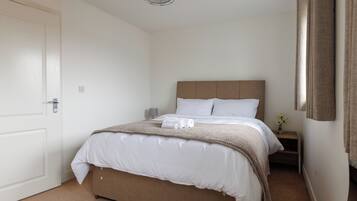 Ein Schlafzimmer mit Bett, Nachttisch, Lampe und einer Tür.