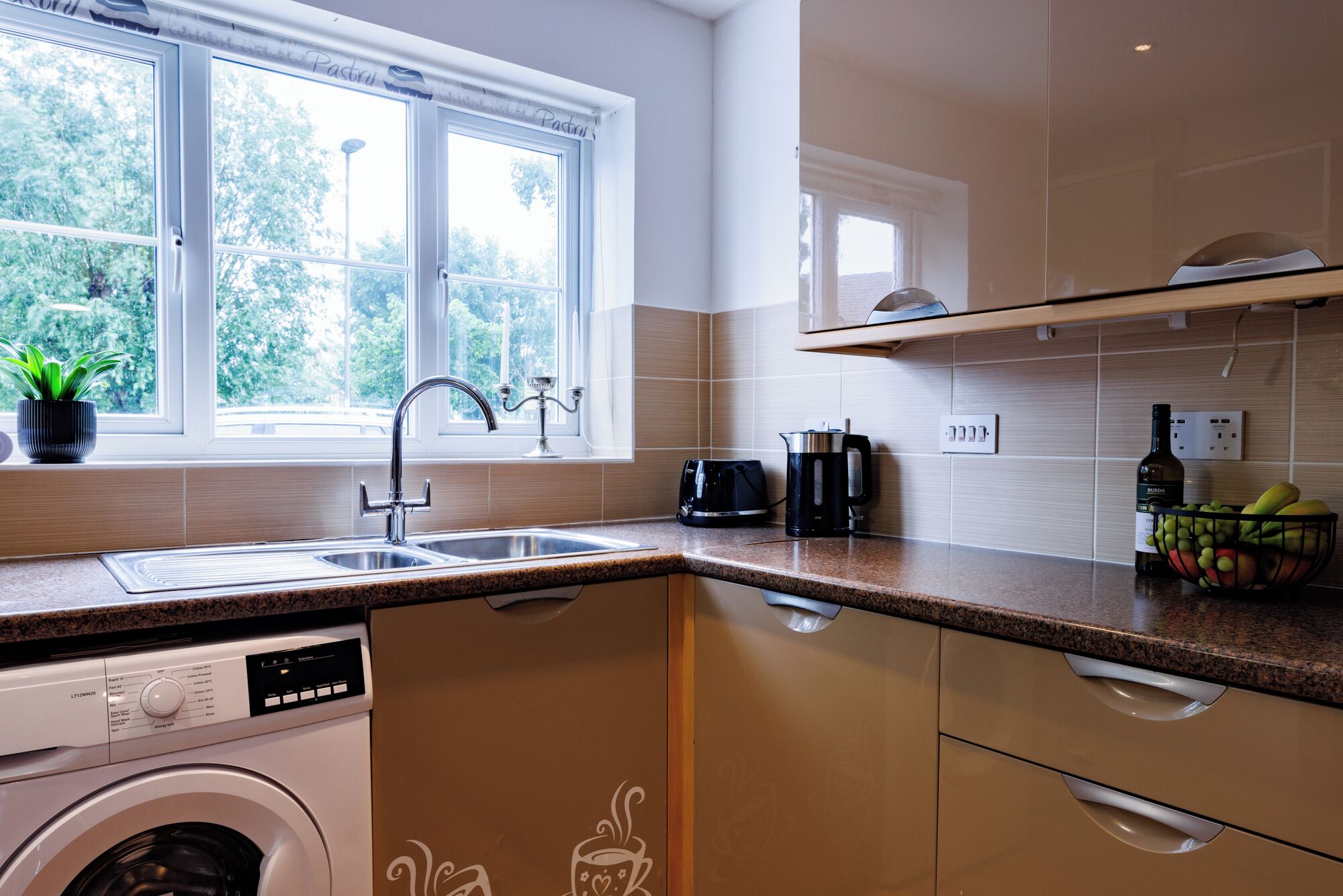 A modern kitchen with a built-in washing machine, a coffee maker, and a fruit basket on the counter.