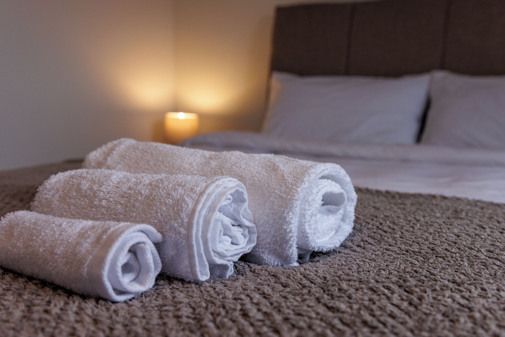 A neatly made bed with white linens and a brown textured blanket.