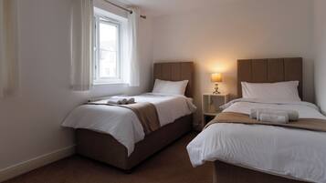 Een hotelkamer met twee bedden, een raam met gordijnen, een bedlampje en een klein plankje.