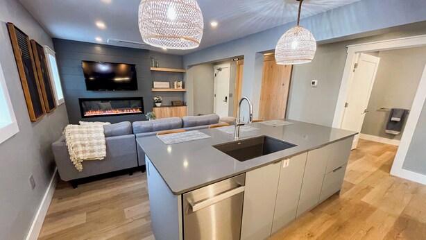 Une cuisine moderne dotée d’un îlot central, d’appareils électroménagers en acier inoxydable et de luminaires suspendus.