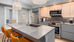 Une cuisine moderne dotée d’un îlot central, d’appareils électroménagers en acier inoxydable et d’un luminaire suspendu.