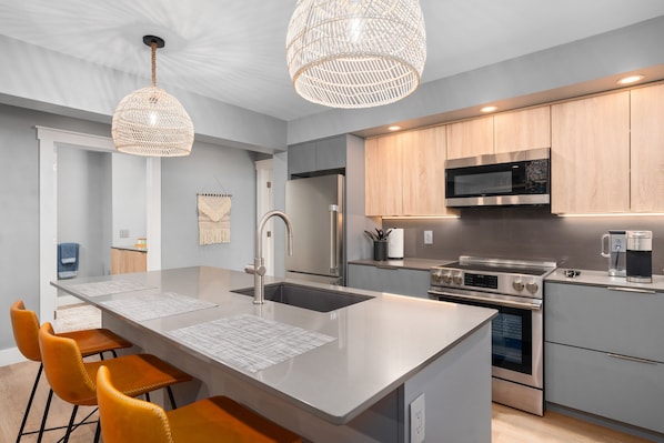 A modern kitchen with a central island, stainless steel appliances, and a hanging light fixture.