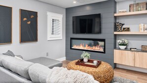 Un salon moderne avec un canapé gris, un téléviseur à écran plat fixé au-dessus d’une cheminée et un meuble en bois agrémenté d’objets décoratifs.