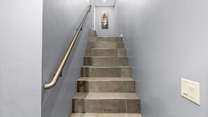 Un escalier avec une rampe métallique, un interrupteur sur le mur et une œuvre d’art encadrée en haut.