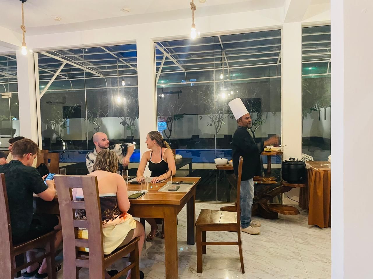 Ein Restaurant mit Holztischen und -stühlen, großen Fenstern und einem modernen Interieur.