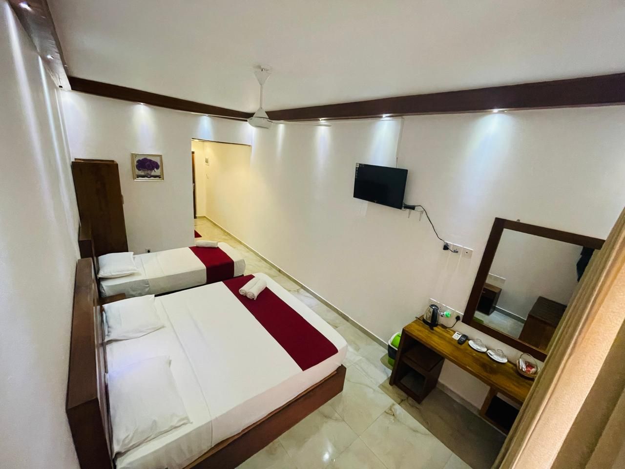 A hotel room with a bed, bedside table, mirror, and a TV mounted on the wall.