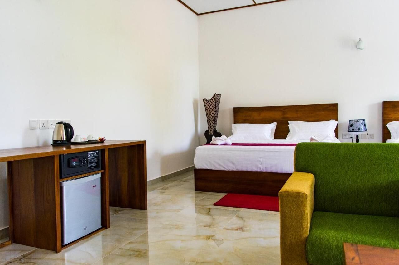 A hotel room with a bed, a small refrigerator, a wooden desk, and a green armchair.
