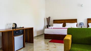 A hotel room with a bed, a small refrigerator, a wooden desk, and a green armchair.