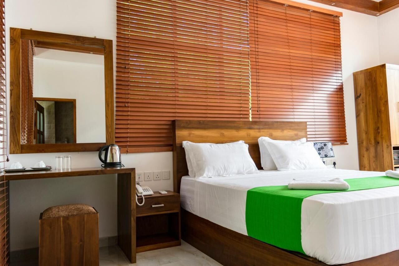 A hotel room with a wooden headboard, a large mirror, a bedside table with a telephone, and a green bedspread.