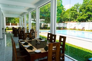 Comedor con vista a una piscina y abundante vegetación.