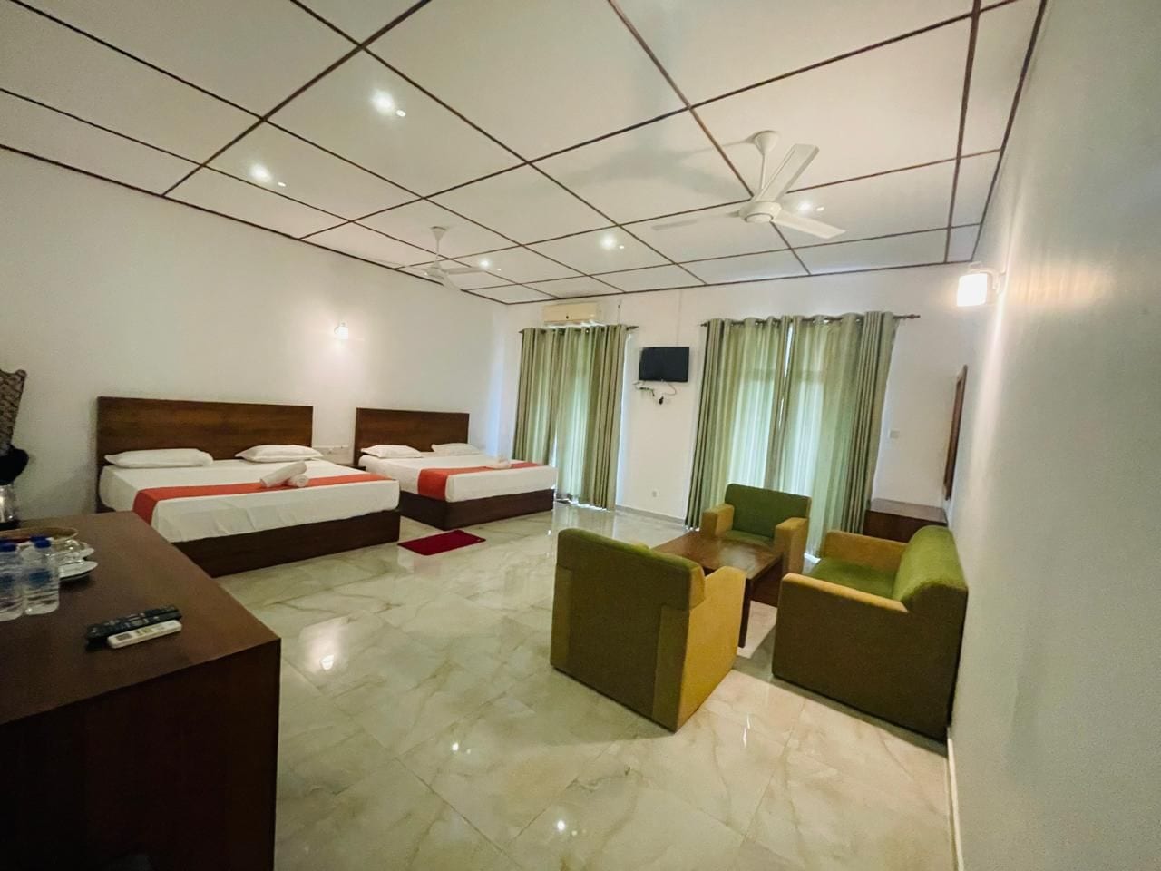 A hotel room with two beds, a desk, a sofa, and a television.
