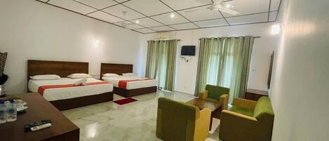 A hotel room with two beds, a desk, a sofa, and a television.