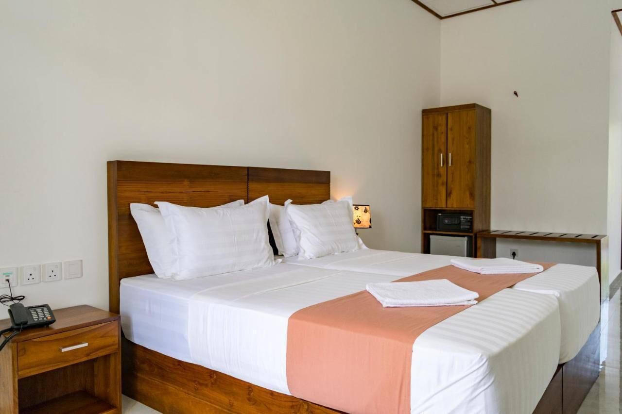 A double bed with white linens and a peach-colored throw, a wooden nightstand with a phone, and a wooden wardrobe in a hotel room.