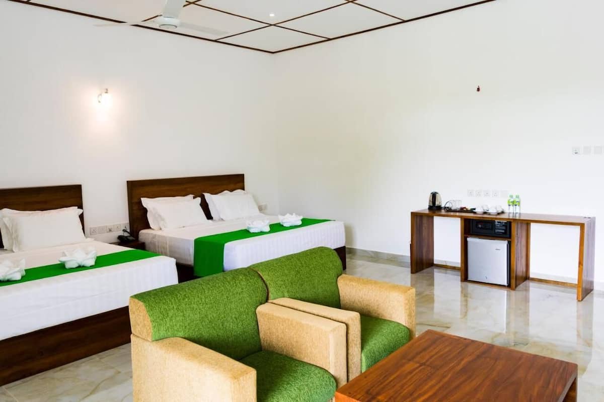 Una habitación de hotel con dos camas, un sofá verde, una mesa de centro de madera y una kitchenette.