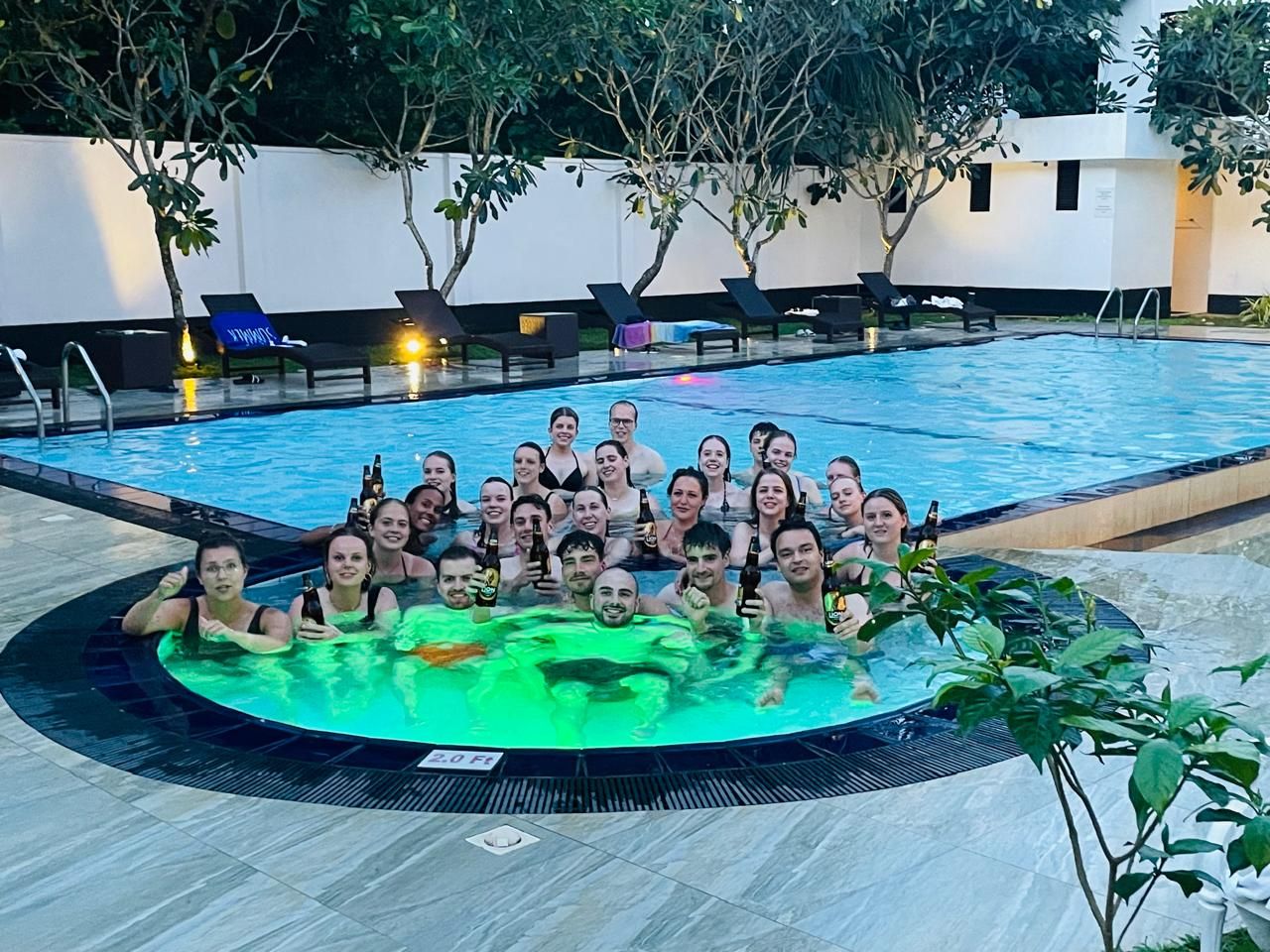 Eine Gruppe von Personen in einem Schwimmbad mit Liegestühlen und einem Whirlpool.