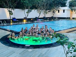 A group of people in a swimming pool with lounge chairs and a hot tub.