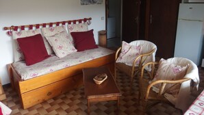 A cozy room with a wooden sofa bed, two wicker chairs, a small wooden table, and a checkered floor. - Coquet Studio (Praz-sur-Arly)
