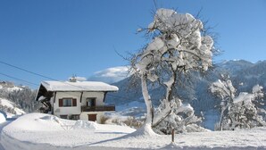 A snow-covered house with a balcony, surrounded by snow-laden trees and mountains in the background. - Coquet Studio (Praz-sur-Arly)