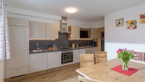 A modern kitchen with white cabinets, a wooden dining table, and a red placemat. - Newly built in 2020, modern furnishings, quiet location, 2 bathrooms, sauna (Ramsau im Zillertal)