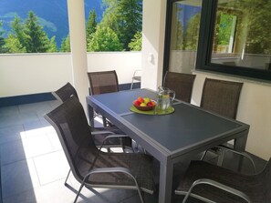 A balcony with a table set for two, featuring a bowl of fruit and a pitcher of water.