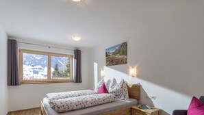 A bedroom with a wooden bed, a view of mountains through a window, a small bedside table, and a chair. - Newly built in 2020, modern furnishings, quiet location, 2 bathrooms, sauna (Ramsau im Zillertal)