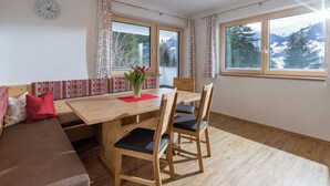 A dining area with a wooden table, chairs, and a vase of flowers. There is a sofa with cushions and a clock on the wall. - Newly built in 2020, modern furnishings, quiet location, 2 bathrooms, sauna (Ramsau im Zillertal)
