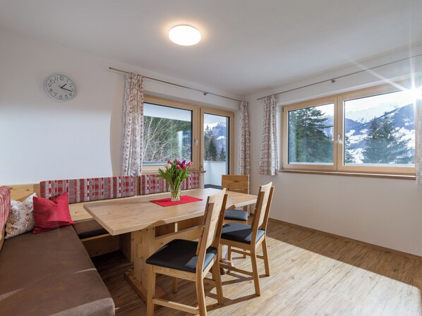 A dining area with a wooden table, chairs, and a vase of flowers. There is a sofa with cushions and a clock on the wall.