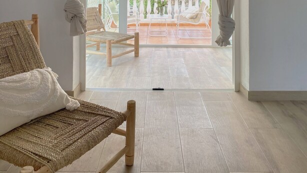 Una habitación con un amplio ventanal de arco, una silla de mimbre, un sofá blanco y un televisor en la pared.