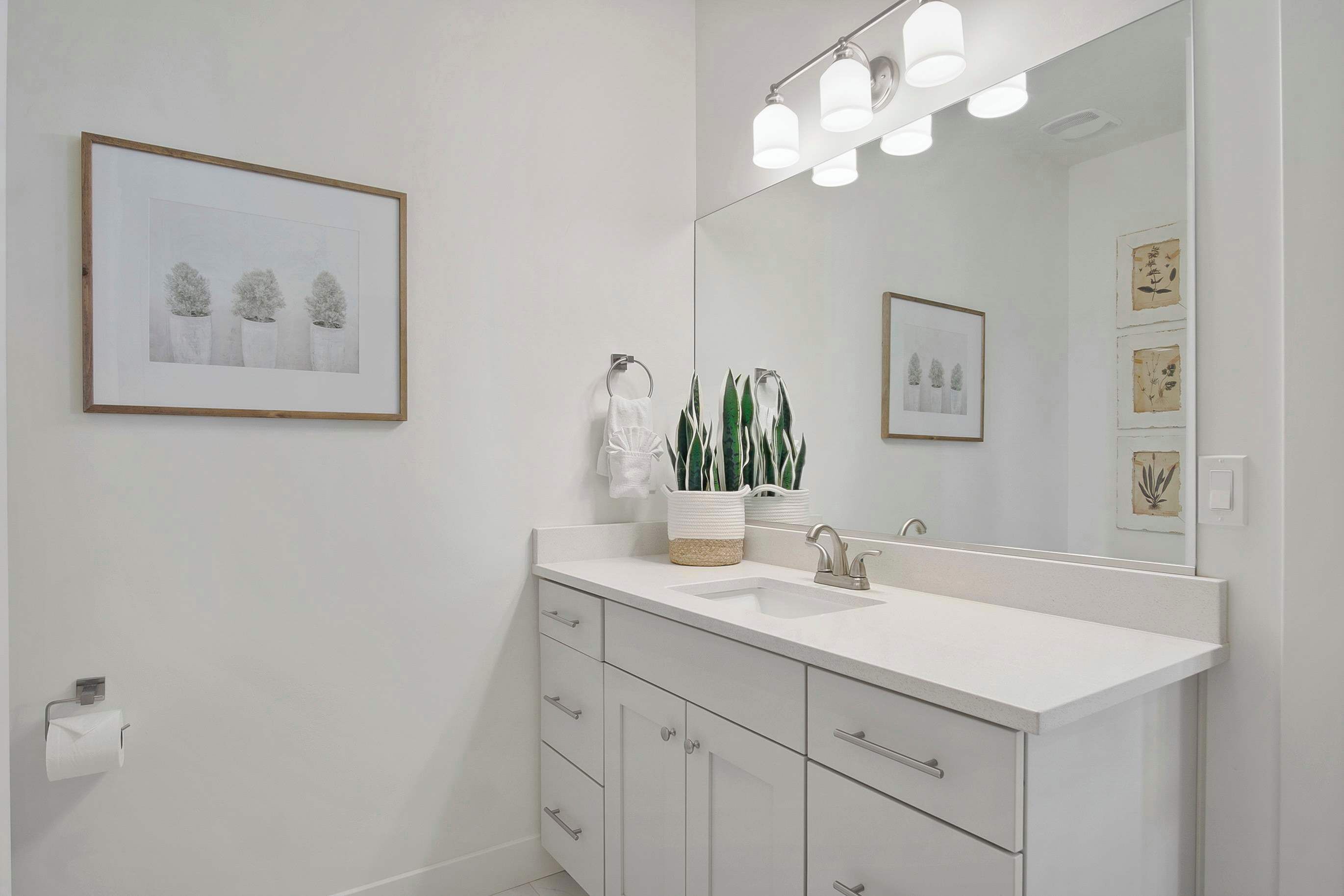 Une salle de bain moderne avec un meuble-lavabo blanc, un grand miroir et des œuvres d’art encadrées accrochées au mur.