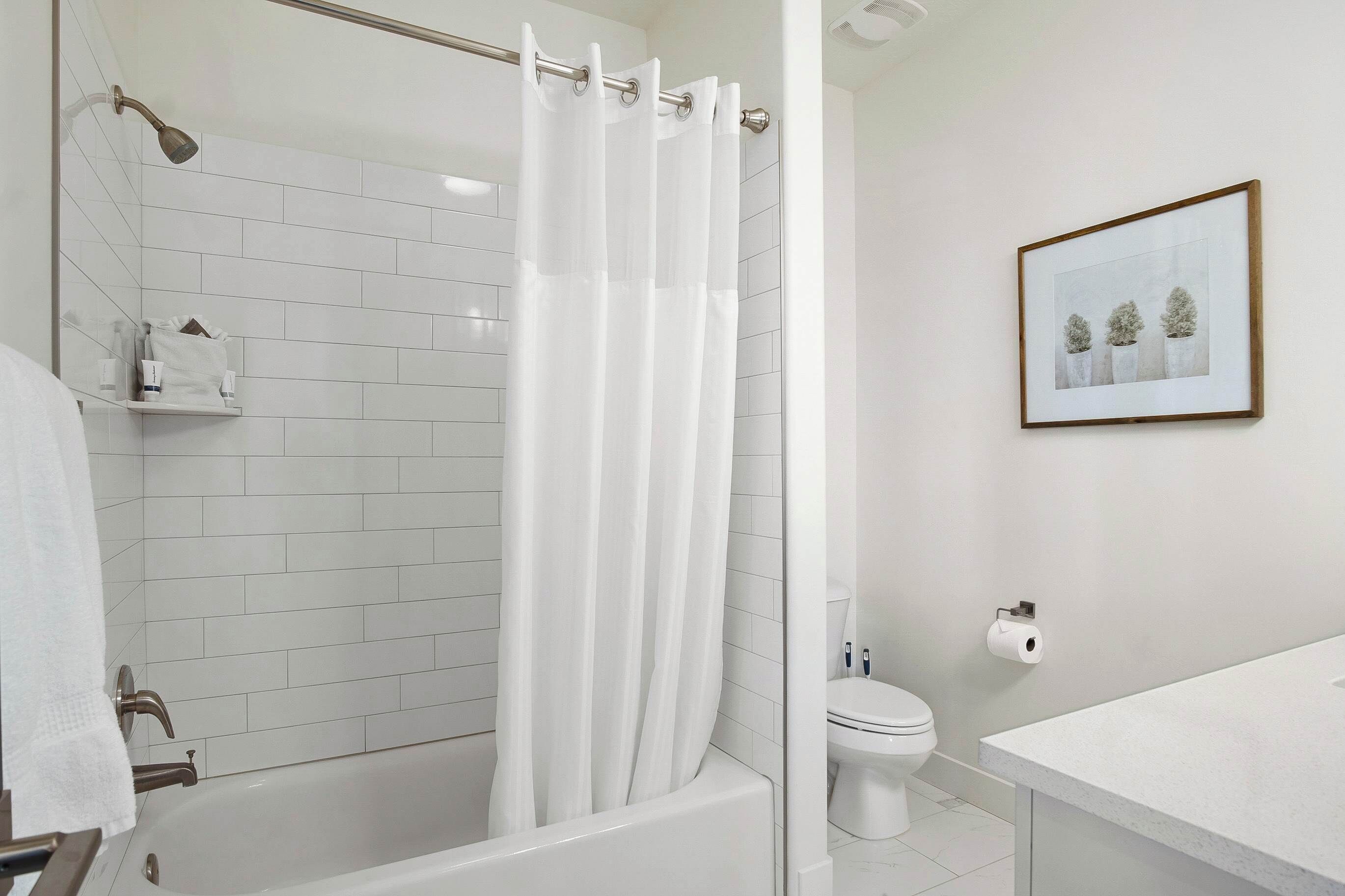 Un baño moderno con ducha de vidrio, azulejos blancos, un inodoro y un cuadro en la pared.